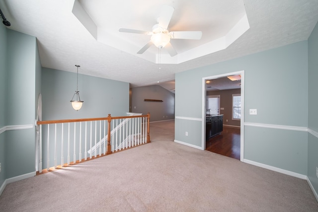 empty room with a raised ceiling, ceiling fan, carpet, and a textured ceiling