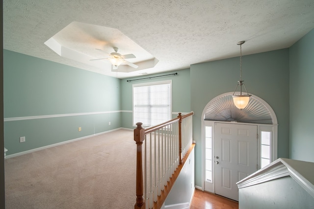 carpeted foyer entrance with ceiling fan, a raised ceiling, and a textured ceiling