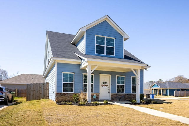 view of front of property with stone siding, a shingled roof, a front lawn, and fence