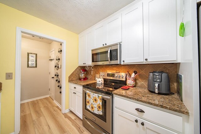 kitchen featuring white cabinetry, dark stone countertops, a textured ceiling, appliances with stainless steel finishes, and light wood-type flooring