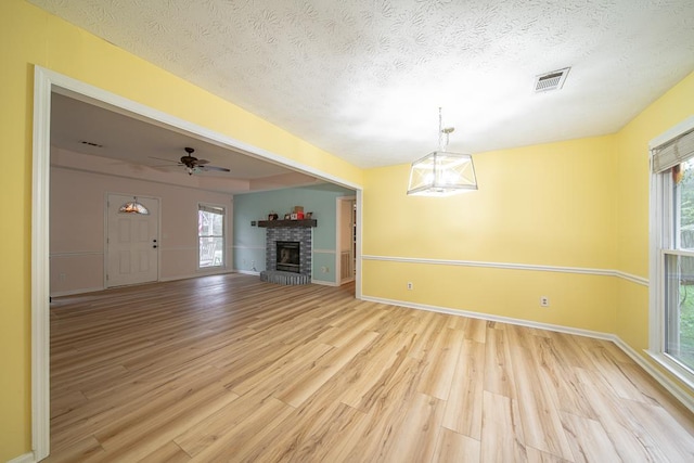 unfurnished living room featuring a fireplace, a textured ceiling, light wood-type flooring, and ceiling fan