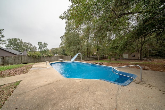 view of pool with a diving board, an outdoor structure, a patio, and a water slide