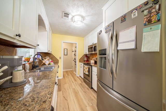 kitchen with sink, dark stone countertops, a textured ceiling, white cabinets, and appliances with stainless steel finishes