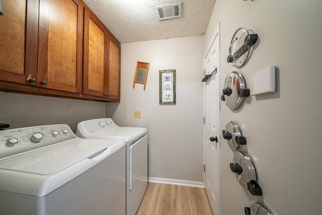 washroom with cabinets, light wood-type flooring, separate washer and dryer, and a textured ceiling