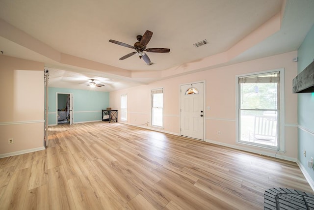 unfurnished living room featuring a raised ceiling, ceiling fan, and light hardwood / wood-style floors