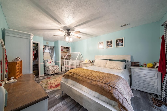 bedroom featuring dark wood-type flooring, a walk in closet, ceiling fan, a textured ceiling, and a closet