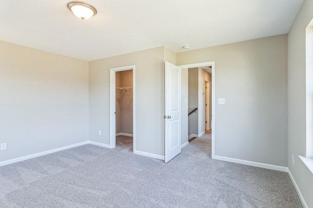 unfurnished bedroom featuring a closet, a walk in closet, and light colored carpet