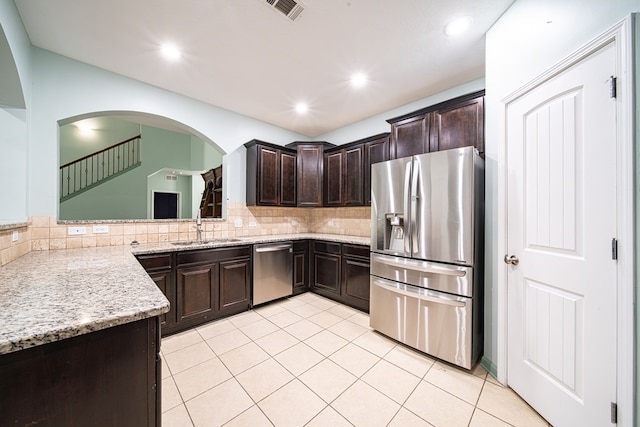 kitchen with light stone counters, dark brown cabinetry, a sink, appliances with stainless steel finishes, and tasteful backsplash