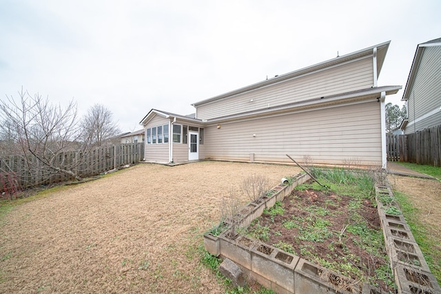 rear view of house featuring driveway, a sunroom, a garden, and fence