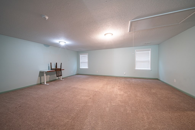 spare room featuring attic access, carpet, a textured ceiling, and baseboards