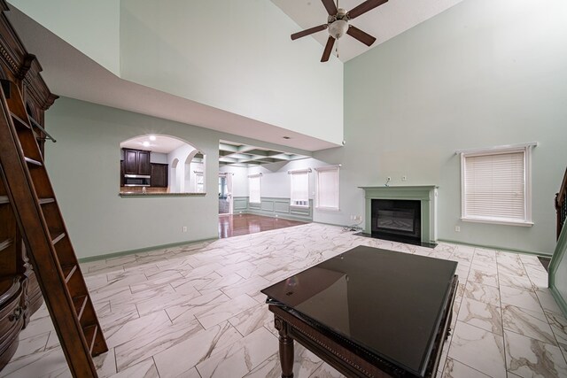 unfurnished living room featuring arched walkways, marble finish floor, a glass covered fireplace, ceiling fan, and baseboards