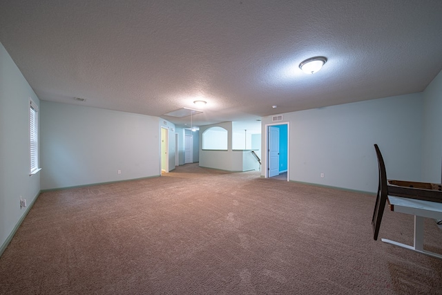 carpeted empty room featuring visible vents, a textured ceiling, and attic access