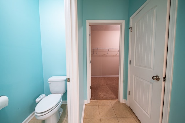 bathroom featuring tile patterned flooring, a walk in closet, baseboards, and toilet