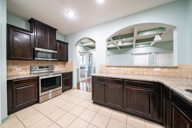 kitchen with appliances with stainless steel finishes, light stone counters, dark brown cabinets, and tasteful backsplash