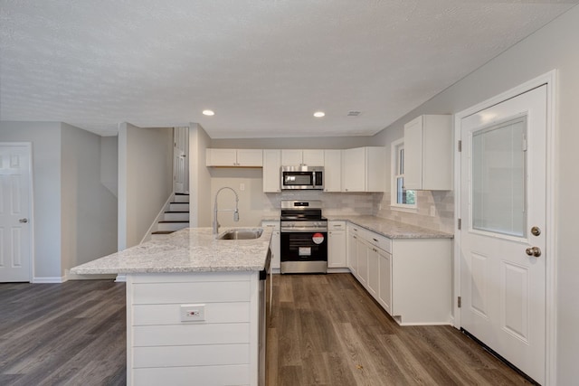 kitchen with a kitchen island with sink, sink, light stone counters, white cabinetry, and stainless steel appliances