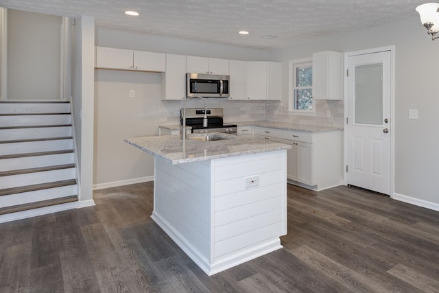 kitchen with a textured ceiling, stainless steel appliances, white cabinets, a center island, and dark hardwood / wood-style floors