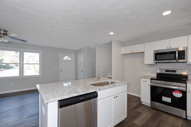 kitchen with stainless steel appliances, dark wood-type flooring, sink, white cabinetry, and an island with sink