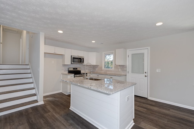 kitchen featuring appliances with stainless steel finishes, backsplash, sink, a center island with sink, and white cabinets