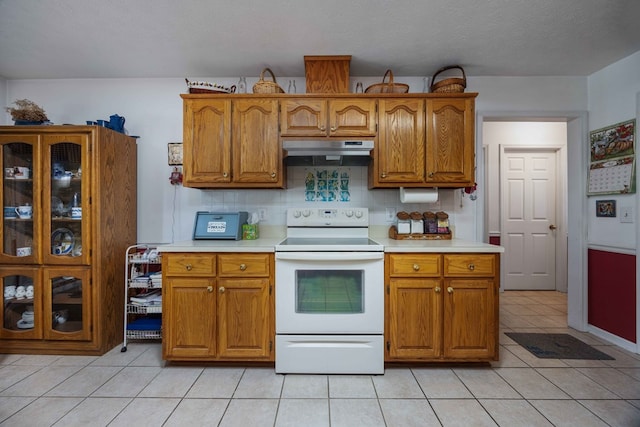 kitchen with under cabinet range hood, white range with electric cooktop, brown cabinets, and light countertops