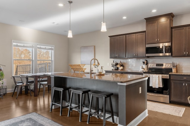 kitchen featuring appliances with stainless steel finishes, pendant lighting, sink, a kitchen breakfast bar, and a center island with sink