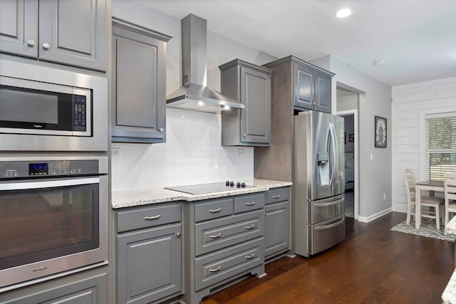 kitchen with appliances with stainless steel finishes, wall chimney exhaust hood, gray cabinets, backsplash, and dark wood finished floors