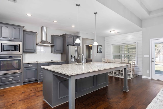 kitchen featuring stainless steel appliances, wall chimney exhaust hood, gray cabinets, a kitchen island with sink, and a sink