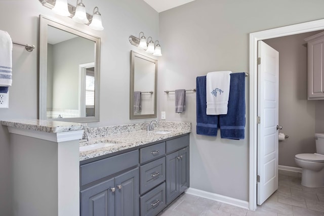 bathroom with toilet, double vanity, baseboards, and tile patterned floors