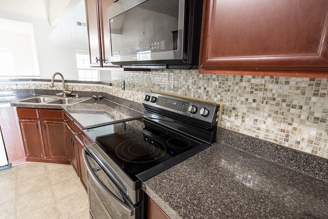 kitchen featuring tasteful backsplash, stainless steel appliances, dark countertops, and a sink