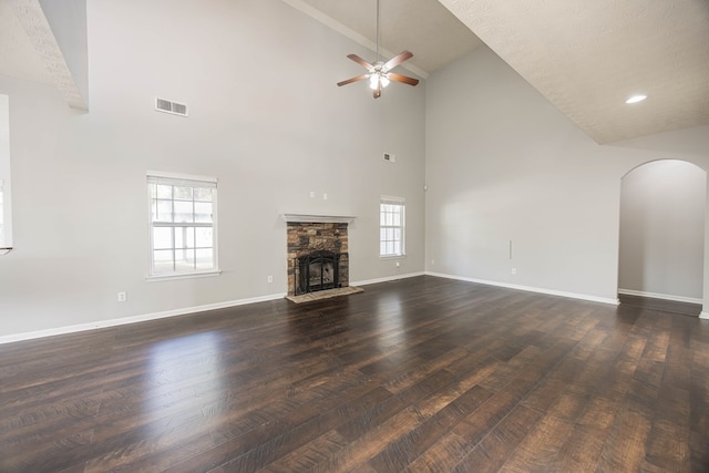 unfurnished living room featuring visible vents, dark wood-type flooring, baseboards, a stone fireplace, and plenty of natural light