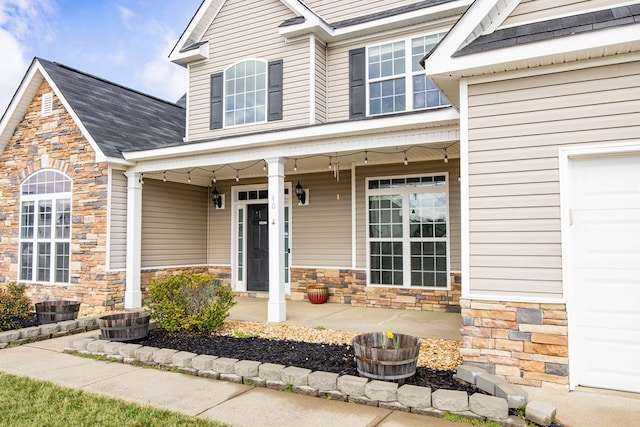 entrance to property with a garage, stone siding, and covered porch