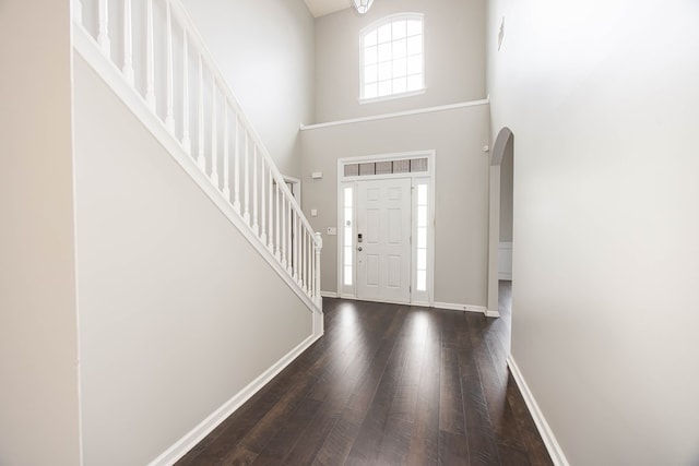 entryway with wood finished floors, baseboards, a high ceiling, arched walkways, and stairs