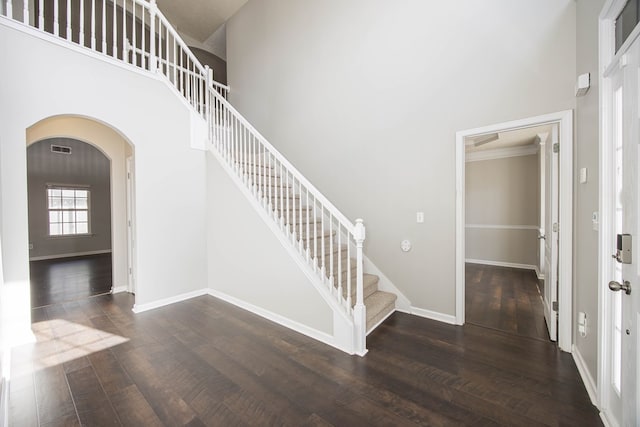 stairway with baseboards, arched walkways, a high ceiling, and wood finished floors