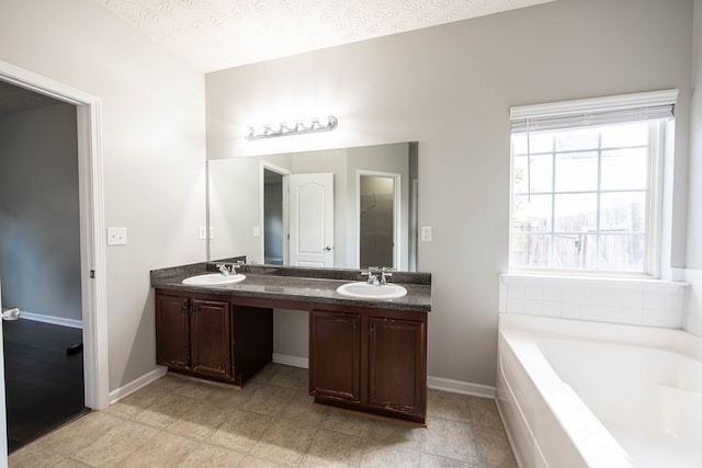 bathroom featuring a textured ceiling, a garden tub, double vanity, and a sink