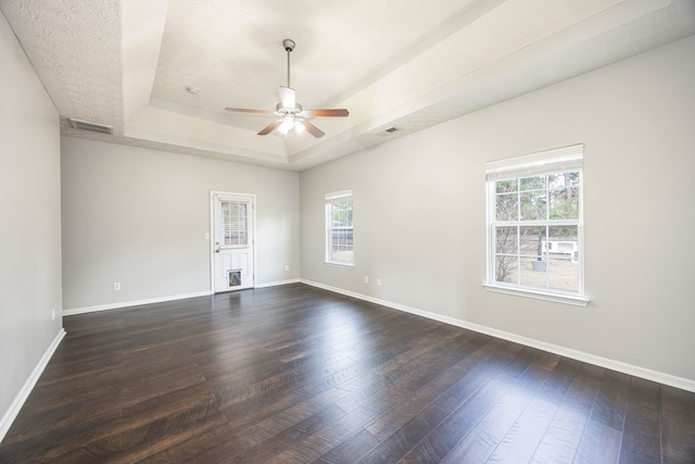 spare room featuring a tray ceiling, baseboards, and dark wood-style flooring