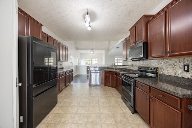 kitchen with tasteful backsplash, dark stone counters, appliances with stainless steel finishes, a peninsula, and a sink