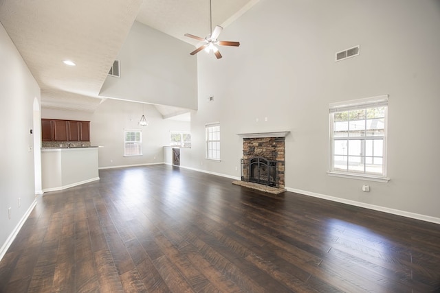 unfurnished living room with a wealth of natural light, dark wood-type flooring, and a stone fireplace