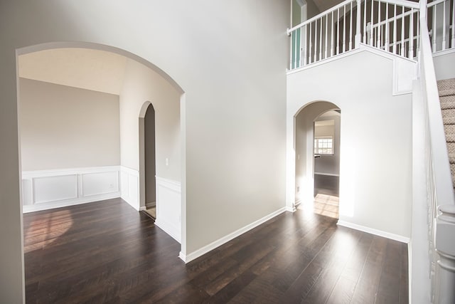 unfurnished room featuring stairs, wood finished floors, a towering ceiling, and wainscoting