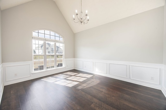 spare room with dark wood-type flooring, a notable chandelier, lofted ceiling, and wainscoting