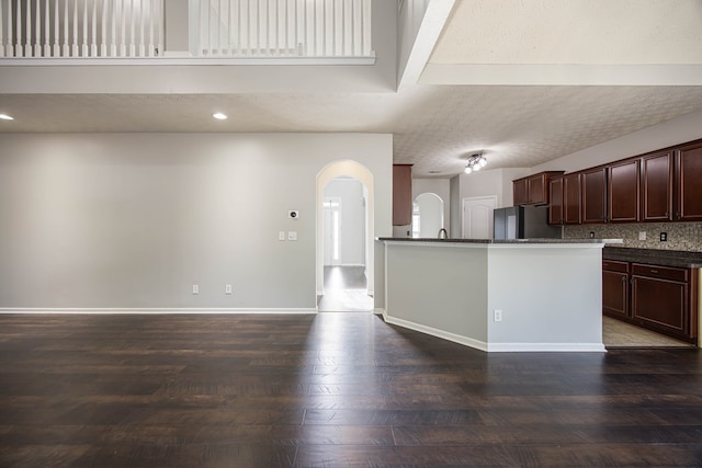 kitchen featuring backsplash, baseboards, arched walkways, refrigerator, and a textured ceiling