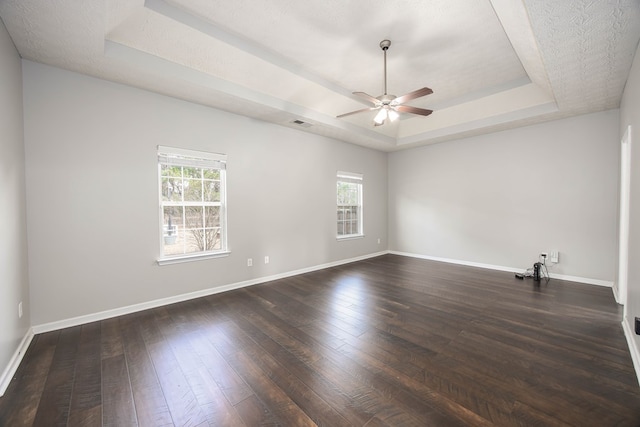 unfurnished room with visible vents, baseboards, a tray ceiling, dark wood-style floors, and a ceiling fan