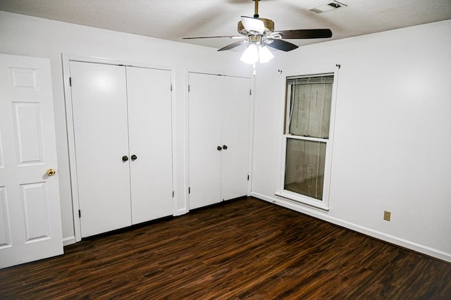 unfurnished bedroom with dark hardwood / wood-style flooring, ceiling fan, and multiple closets