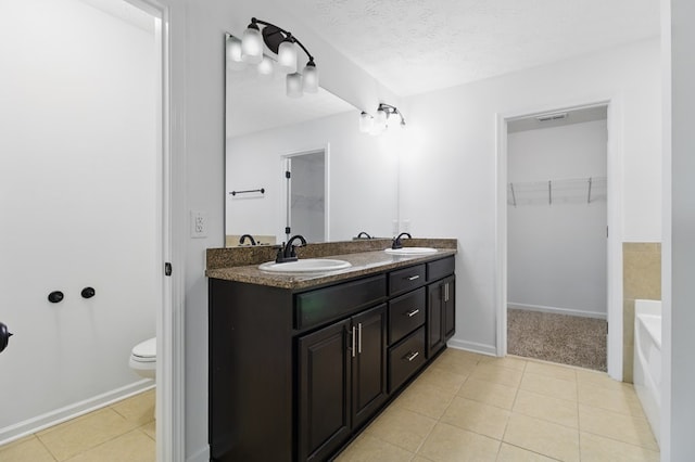 full bath featuring a walk in closet, double vanity, tile patterned floors, toilet, and a textured ceiling