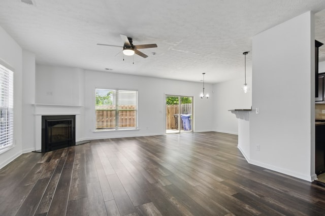 unfurnished living room with a glass covered fireplace, a ceiling fan, dark wood-style flooring, a chandelier, and baseboards