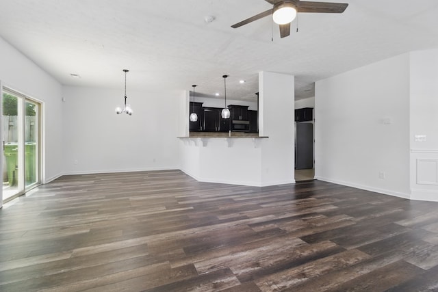 unfurnished living room with ceiling fan, dark wood-style floors, a chandelier, and baseboards
