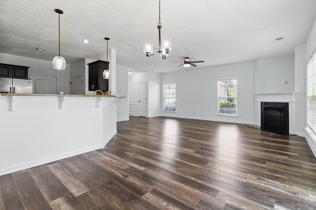 unfurnished living room with ceiling fan, dark wood-style flooring, a fireplace, a chandelier, and baseboards