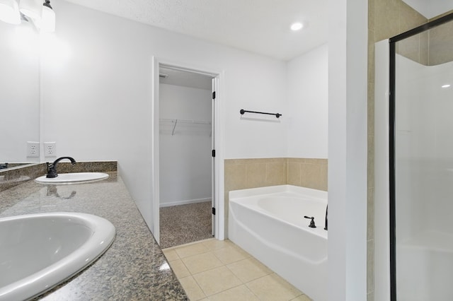 bathroom with tile patterned flooring, a walk in closet, a bath, a shower stall, and double vanity