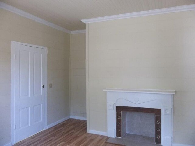 unfurnished living room with wood-type flooring, crown molding, and a tiled fireplace