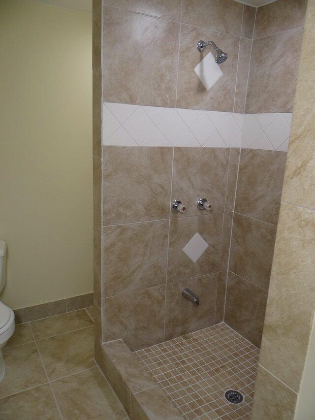 bathroom featuring tile patterned flooring, toilet, and a tile shower