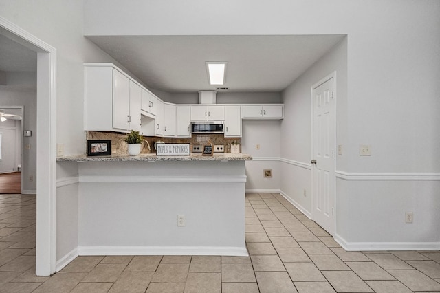 kitchen with a peninsula, tasteful backsplash, stainless steel microwave, and white cabinets