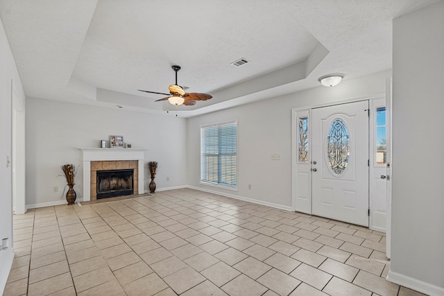 foyer entrance featuring a tile fireplace, a raised ceiling, a textured ceiling, and baseboards